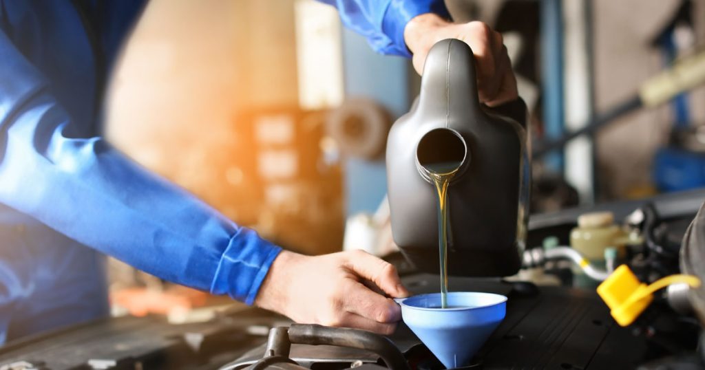 Hyundai service technician performing an oil change service and pouring new oil into a vehicle engine.