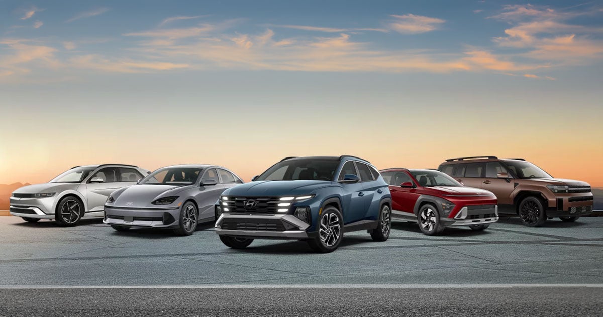 A lineup of five Hyundai vehicles parked side-by-side from left to right: the Hyundai Ioniq 5 (silver electric crossover), the Hyundai Ioniq 6 (silver electric sedan), the Hyundai Tucson (blue compact SUV), the Hyundai Kona (red subcompact SUV), and the Hyundai Santa Fe (bronze midsize SUV).